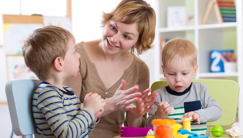Woman and kids boys with play clay toys at day care center